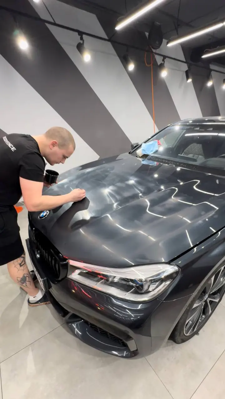 Мастер натягивает пленку на капот BMW